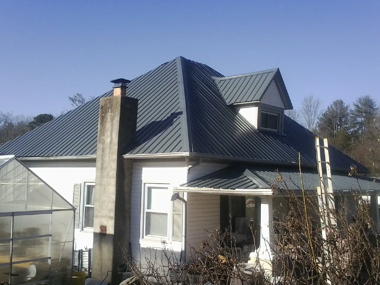 Dark blue standing seam metal roof on a white farmhouse with dormer — Slate & Tile Roof Repair by Roofing Brothers in Upper Marlboro