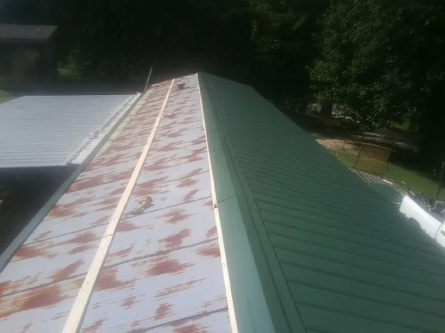 Old rusted panels beside newly installed green metal roofing — Wind Damage Roof Repair by Roofing Brothers in Upper Marlboro