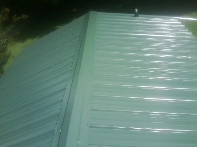 New green metal panels meeting at the ridge of a roof — Flat Roof Repair work by our crew in Upper Marlboro