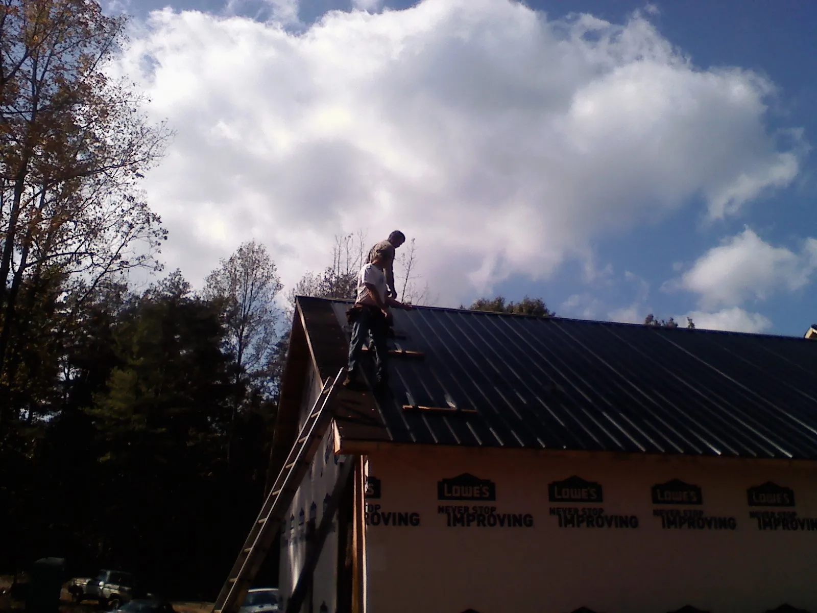 Roofer fastening dark metal panels high against a cloudy sky, from a Roof Inspection job in Upper Marlboro